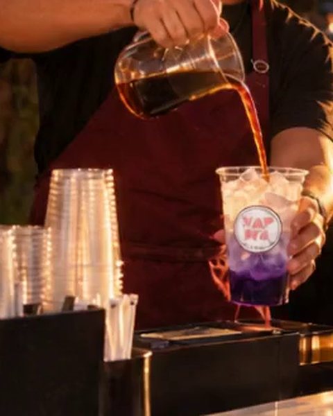 Close-up of cold brew being poured over ice and ube into a Kapwa Coffee Bar cup and handed to a customer